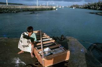 Niño con periódico en un muelle de islas Galápagos
