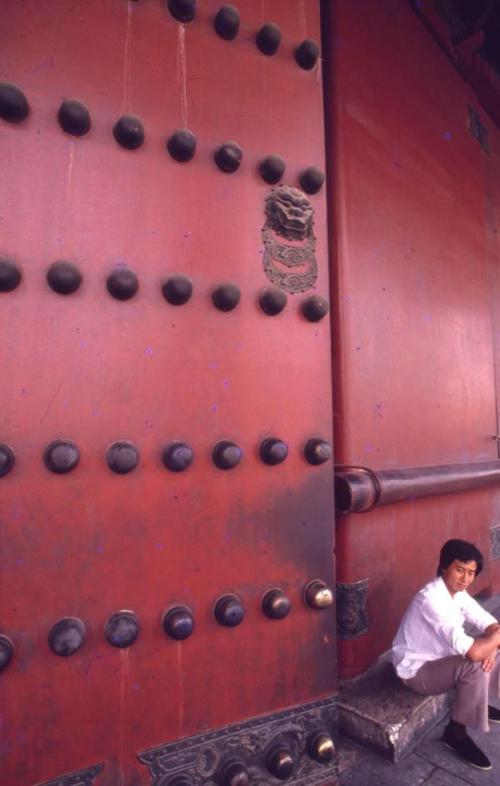 Joven sentado cerca de una puerta de la Ciudad Prohibida, Pekín