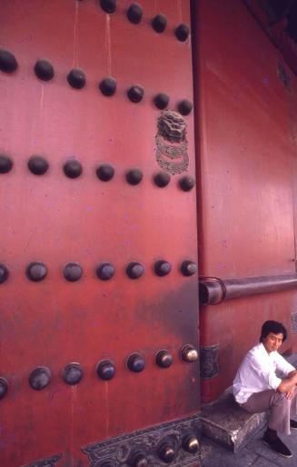 Joven sentado cerca de una puerta de la Ciudad Prohibida, Pekín