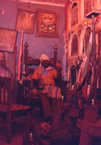 Sacerdote de vudú dominicano con bandera de Papá Candelo entre santos Petró